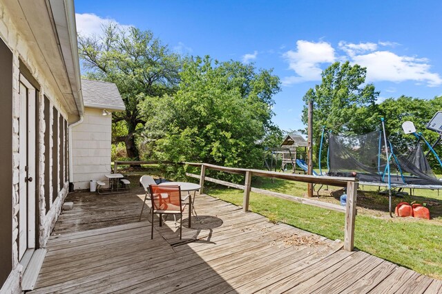 wooden terrace with a yard, a trampoline, outdoor dining area, and a playground