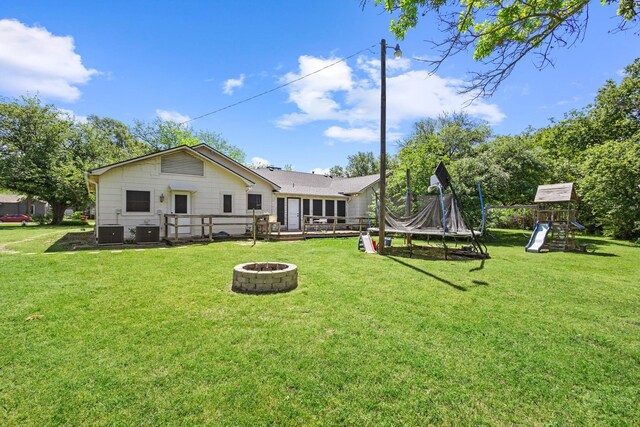 back of house featuring a lawn, an outdoor fire pit, central air condition unit, and a playground