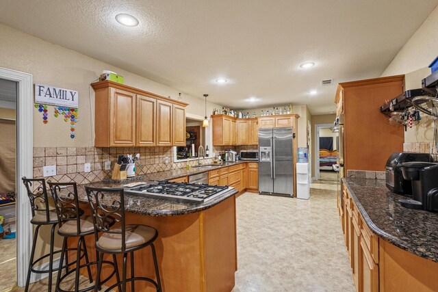 kitchen featuring stainless steel appliances, a peninsula, a sink, tasteful backsplash, and visible vents