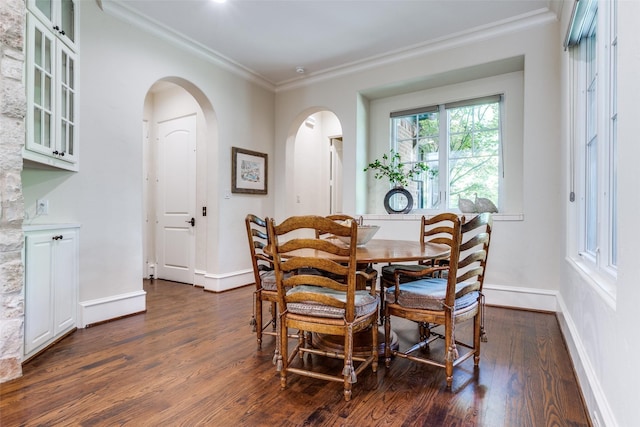 dining room featuring arched walkways, crown molding, dark wood-style flooring, and baseboards