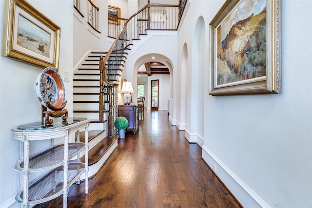 foyer with baseboards, stairway, a high ceiling, dark wood finished floors, and arched walkways