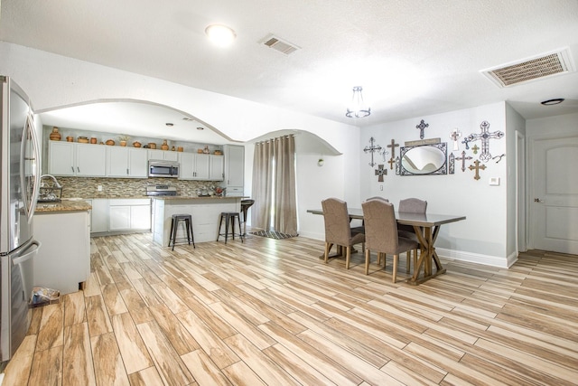 dining room featuring arched walkways, light wood finished floors, visible vents, and baseboards