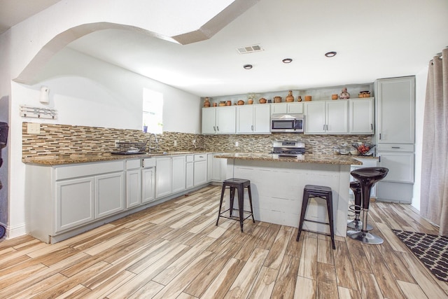kitchen with stainless steel appliances, light wood finished floors, visible vents, and backsplash