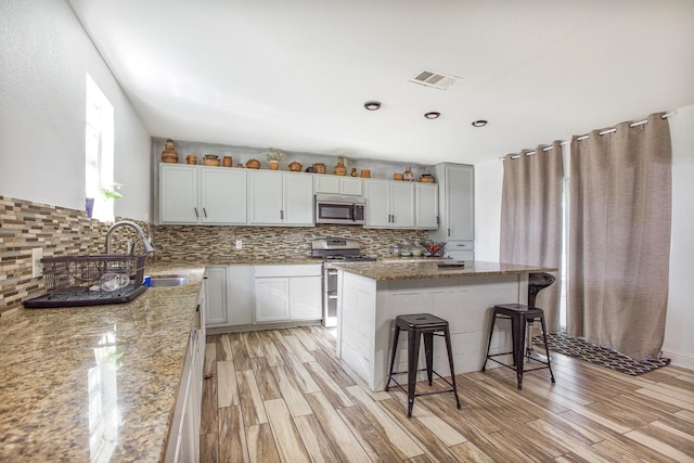 kitchen featuring a breakfast bar, light stone countertops, visible vents, decorative backsplash, and appliances with stainless steel finishes