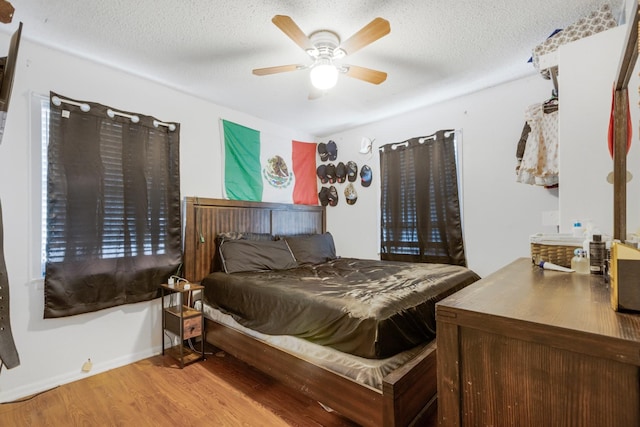 bedroom featuring ceiling fan, a textured ceiling, baseboards, and wood finished floors