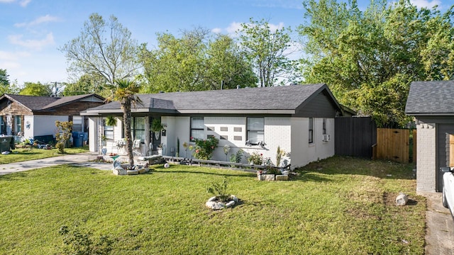 ranch-style home featuring roof with shingles, a front yard, brick siding, and fence