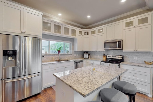 kitchen featuring stainless steel appliances, a sink, crown molding, a breakfast bar area, and dark wood-style floors