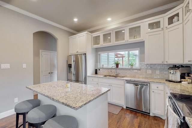 kitchen with stainless steel appliances, a sink, crown molding, a breakfast bar, and arched walkways