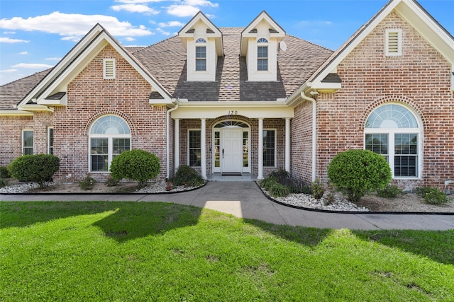 view of front of property with roof with shingles, a front yard, and brick siding