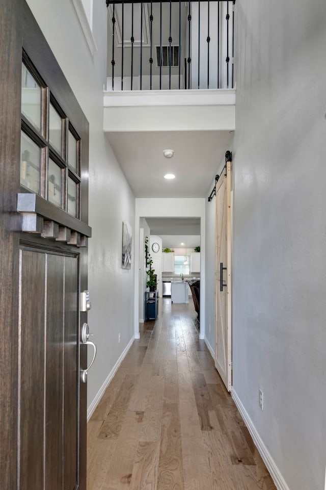 entrance foyer featuring a barn door, a high ceiling, wood finished floors, visible vents, and baseboards