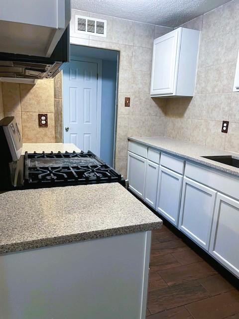 3915 Mather Ct, Dallas, TX 75211 - kitchen featuring tile walls, extractor fan, dark wood-type flooring, gas stove, and white cabinets