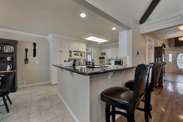 kitchen with a kitchen breakfast bar, dark countertops, white cabinets, visible vents, and appliances with stainless steel finishes
