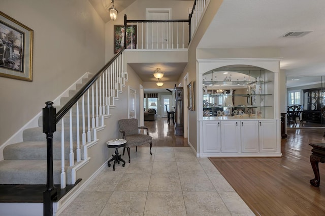 entryway with light wood-type flooring, baseboards, a high ceiling, stairs, and visible vents