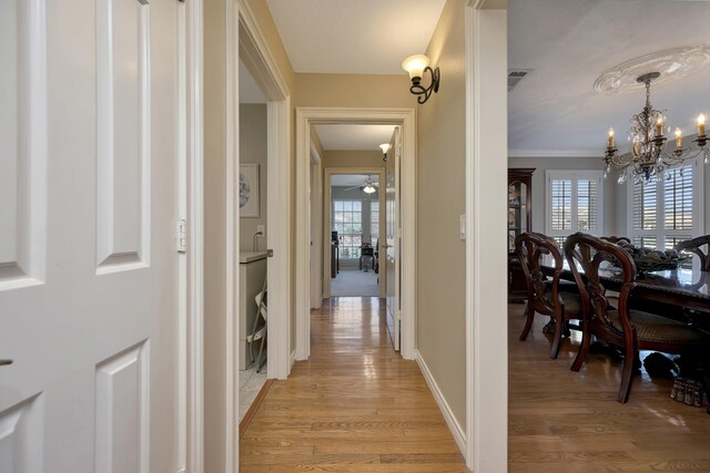 hall with baseboards, an inviting chandelier, crown molding, light wood-style floors, and visible vents