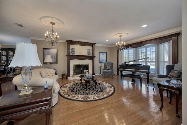 living room featuring visible vents, an inviting chandelier, a fireplace, crown molding, and wood finished floors