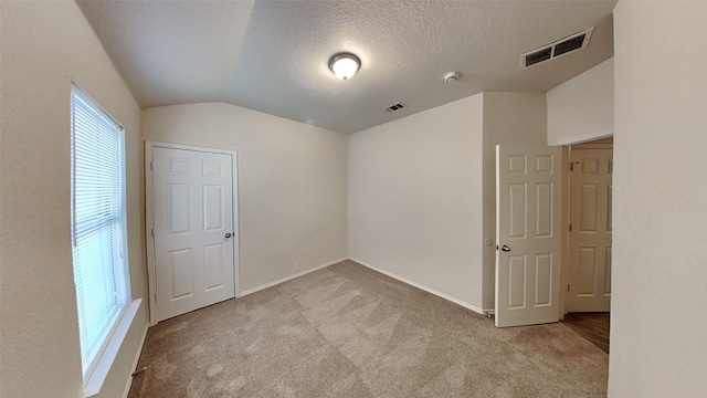 carpeted empty room with visible vents, a textured ceiling, baseboards, and lofted ceiling