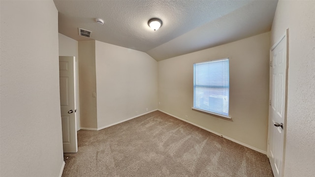 carpeted spare room with a textured ceiling, visible vents, baseboards, and lofted ceiling