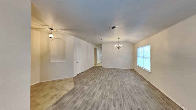 empty room with wood finished floors, an inviting chandelier, lofted ceiling, and visible vents