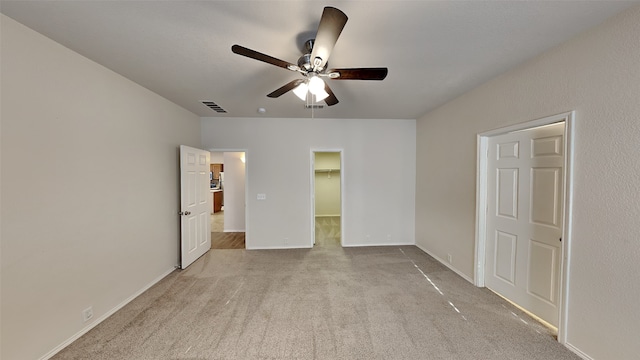 unfurnished bedroom with baseboards, carpet flooring, a walk in closet, visible vents, and ceiling fan