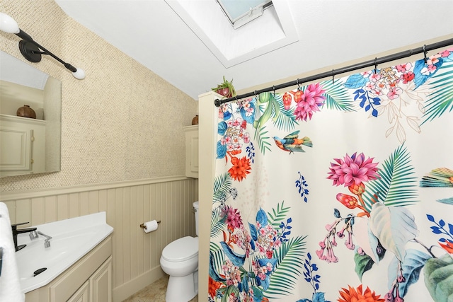 bathroom featuring vanity, toilet, a wainscoted wall, curtained shower, and lofted ceiling with skylight