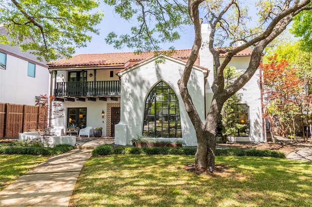mediterranean / spanish house with a tiled roof, stucco siding, a front lawn, and a balcony