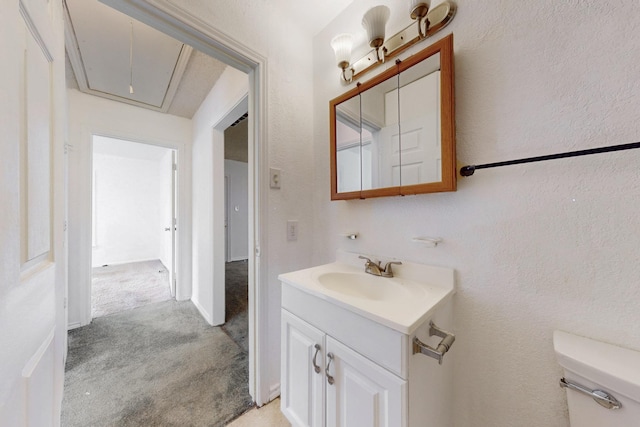 half bathroom featuring a textured wall, toilet, and vanity