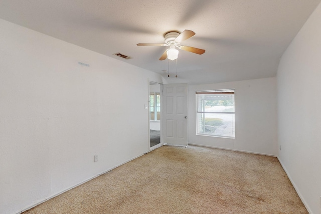 spare room featuring light carpet, a ceiling fan, visible vents, and baseboards
