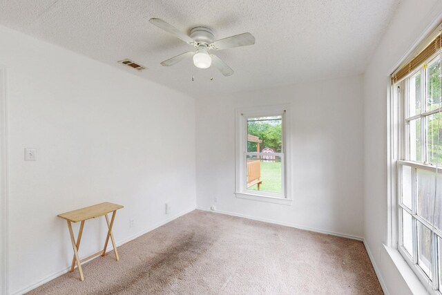 carpeted spare room featuring baseboards, a ceiling fan, a textured ceiling, and visible vents
