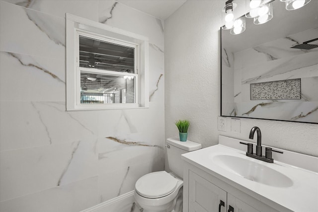 bathroom with a textured wall, toilet, vanity, and a marble finish shower