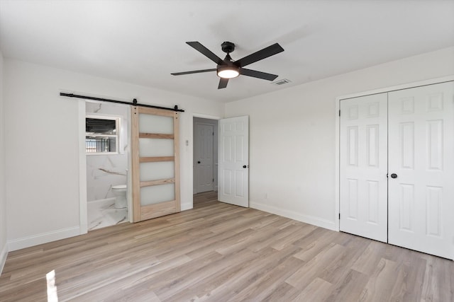 unfurnished bedroom with a barn door, a closet, light wood finished floors, baseboards, and visible vents