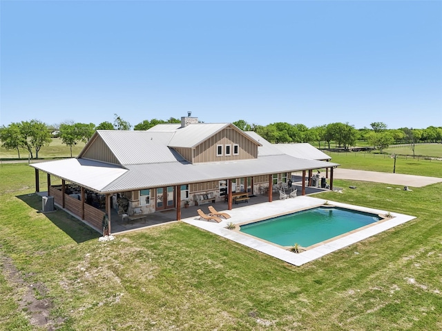 back of property with central AC, a patio area, metal roof, an outdoor pool, and a chimney