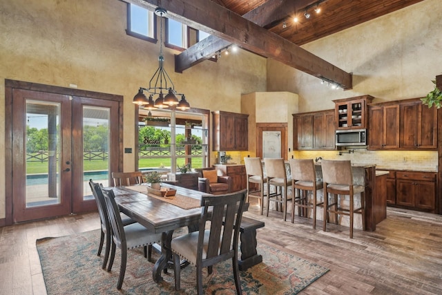 dining area featuring track lighting, wood-type flooring, beamed ceiling, french doors, and high vaulted ceiling
