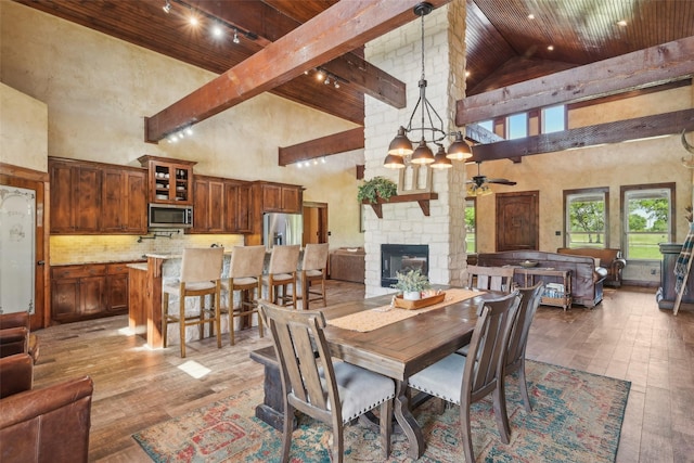 dining area with a stone fireplace, high vaulted ceiling, wooden ceiling, and hardwood / wood-style flooring