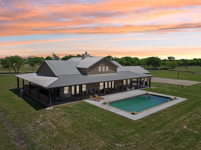 back of house at dusk with a patio area, an outdoor pool, a lawn, and metal roof