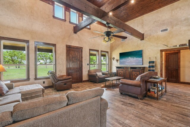 living area with ceiling fan, a high ceiling, wood finished floors, baseboards, and beam ceiling