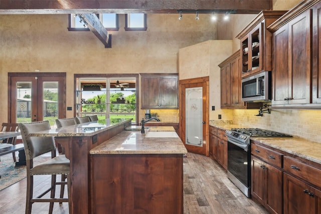 kitchen featuring a towering ceiling, a breakfast bar, stainless steel appliances, hardwood / wood-style flooring, and a sink