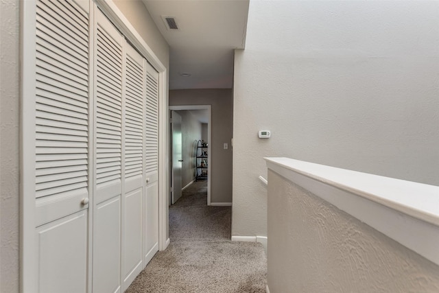 hall featuring visible vents, baseboards, and light colored carpet