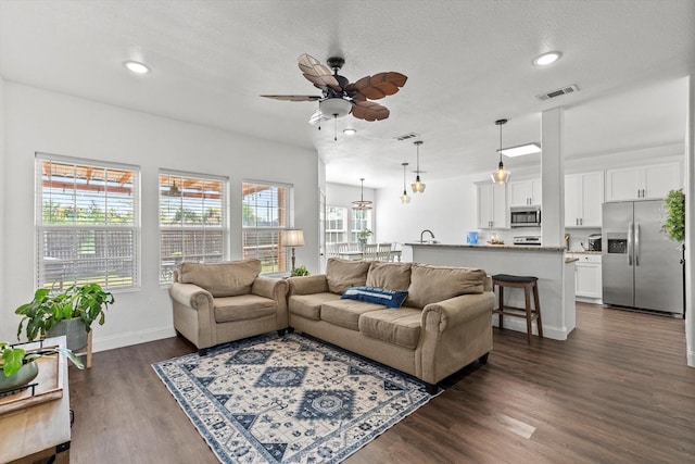 living area with dark wood-type flooring, visible vents, baseboards, and ceiling fan