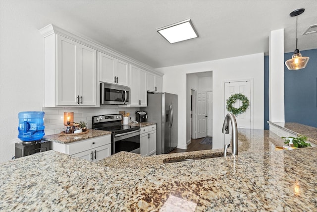 kitchen with white cabinets, a sink, appliances with stainless steel finishes, light stone countertops, and backsplash