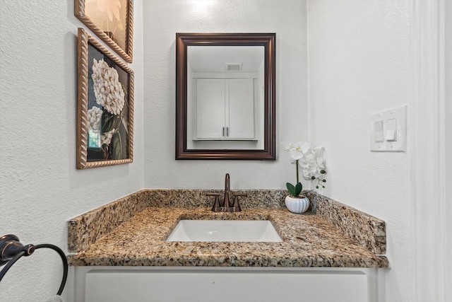 bathroom with visible vents, vanity, and a textured wall