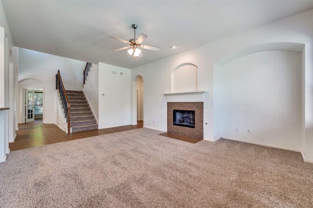 unfurnished living room with arched walkways, carpet, ceiling fan, stairway, and a tiled fireplace