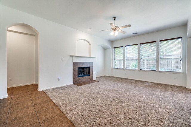 unfurnished living room with ceiling fan, a tiled fireplace, baseboards, tile patterned floors, and carpet floors