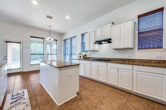 kitchen featuring under cabinet range hood, black gas cooktop, a center island, white cabinets, and dark stone countertops