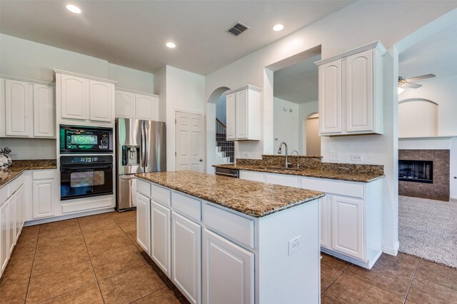 kitchen featuring black appliances, a sink, a center island, arched walkways, and white cabinets