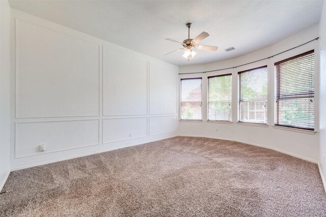 carpeted spare room with ceiling fan and a decorative wall