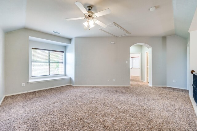 carpeted spare room featuring attic access, a ceiling fan, arched walkways, vaulted ceiling, and a smoke detector