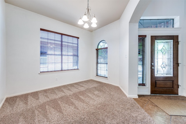 carpeted foyer featuring a chandelier and baseboards