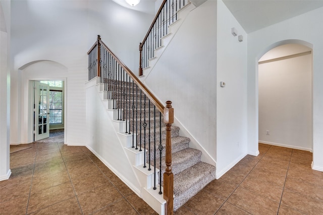 stairs with arched walkways, tile patterned flooring, a towering ceiling, and baseboards