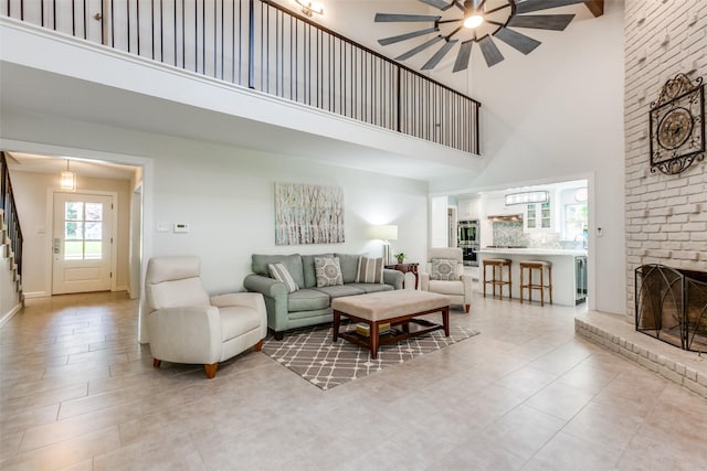 living room with a brick fireplace, a high ceiling, and a ceiling fan