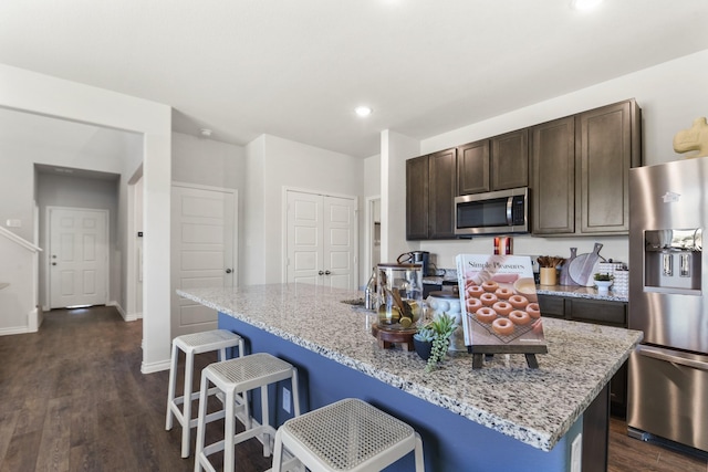 kitchen with dark brown cabinets, dark wood-style flooring, stainless steel appliances, and a kitchen bar